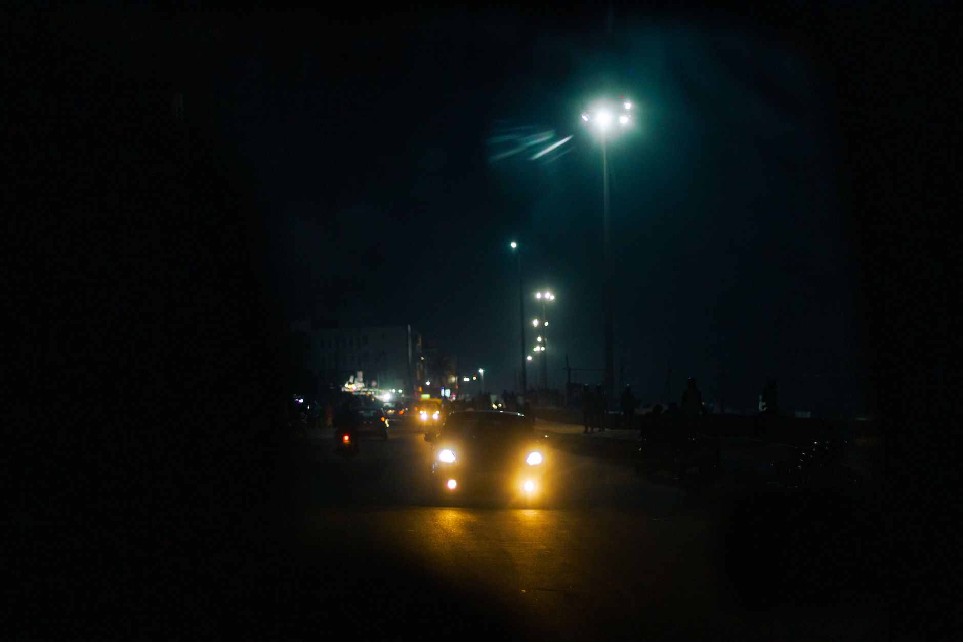 Carro com os faróis acesos numa avenida à noite