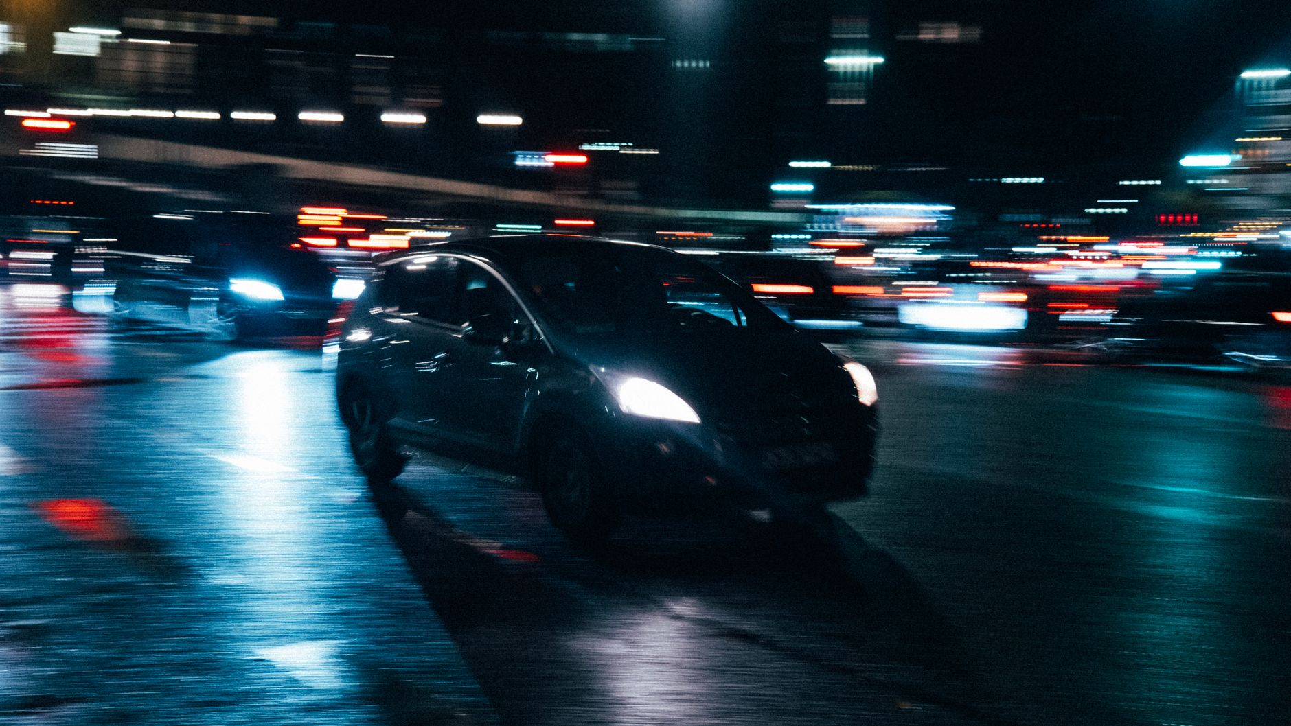 Carro em marcha numa rua da cidade à noite, com as luzes a rasgar o escuro